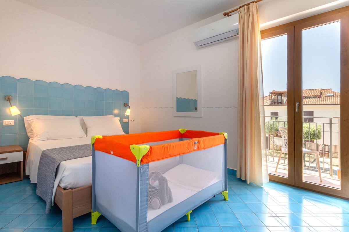 Ein Schlafzimmer mit Bett, Babyreisebett, Nachttisch und Blick auf den Balkon.