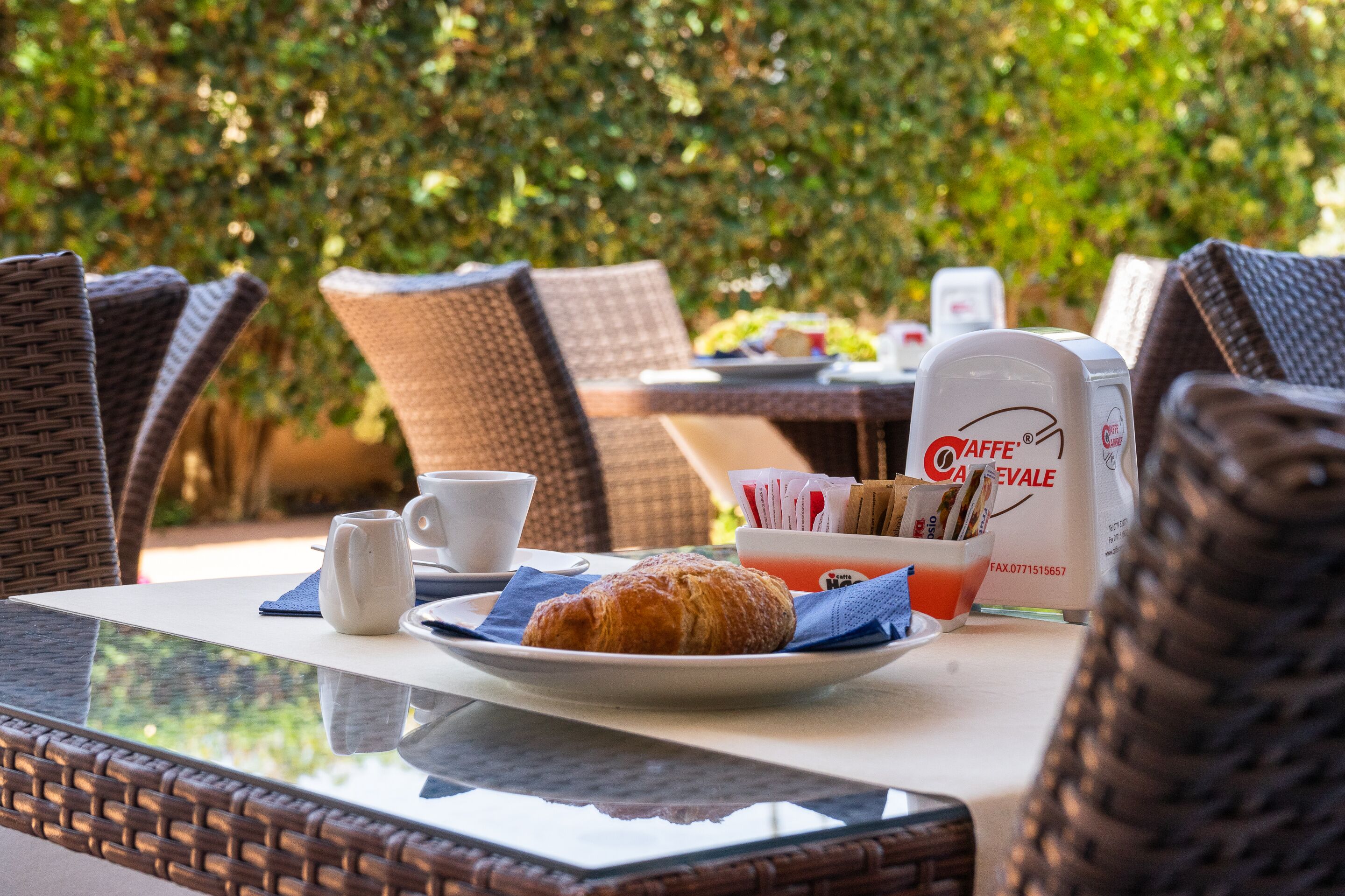 A breakfast table with a croissant, coffee cups, and a coffee maker.