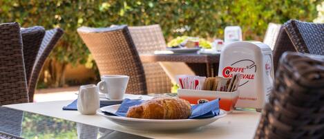 A breakfast table with a croissant, coffee cups, and a coffee maker.