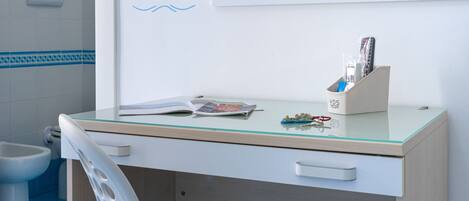 A bathroom with a white toilet, a bidet, and a glass-topped desk with a book and remote controls.
