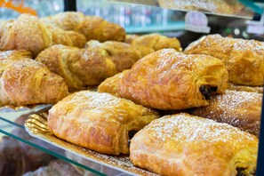 Eine Auswahl an Gebäck, darunter Croissants und Blätterteigtaschen, präsentiert auf einer Glasablage.