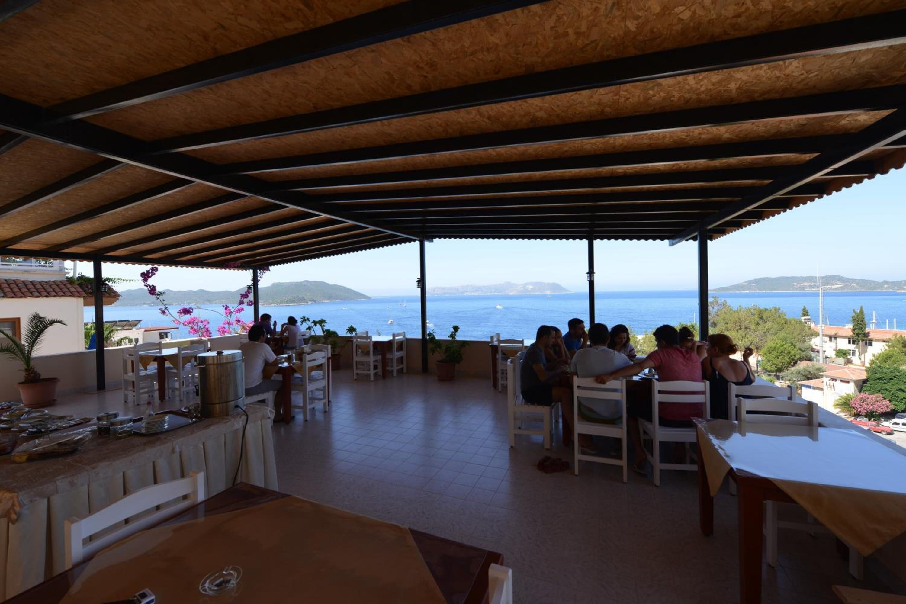 Un espace de restauration en plein air offrant une vue sur la mer, abrité par un toit en bois et aménagé avec des tables et des chaises blanches.