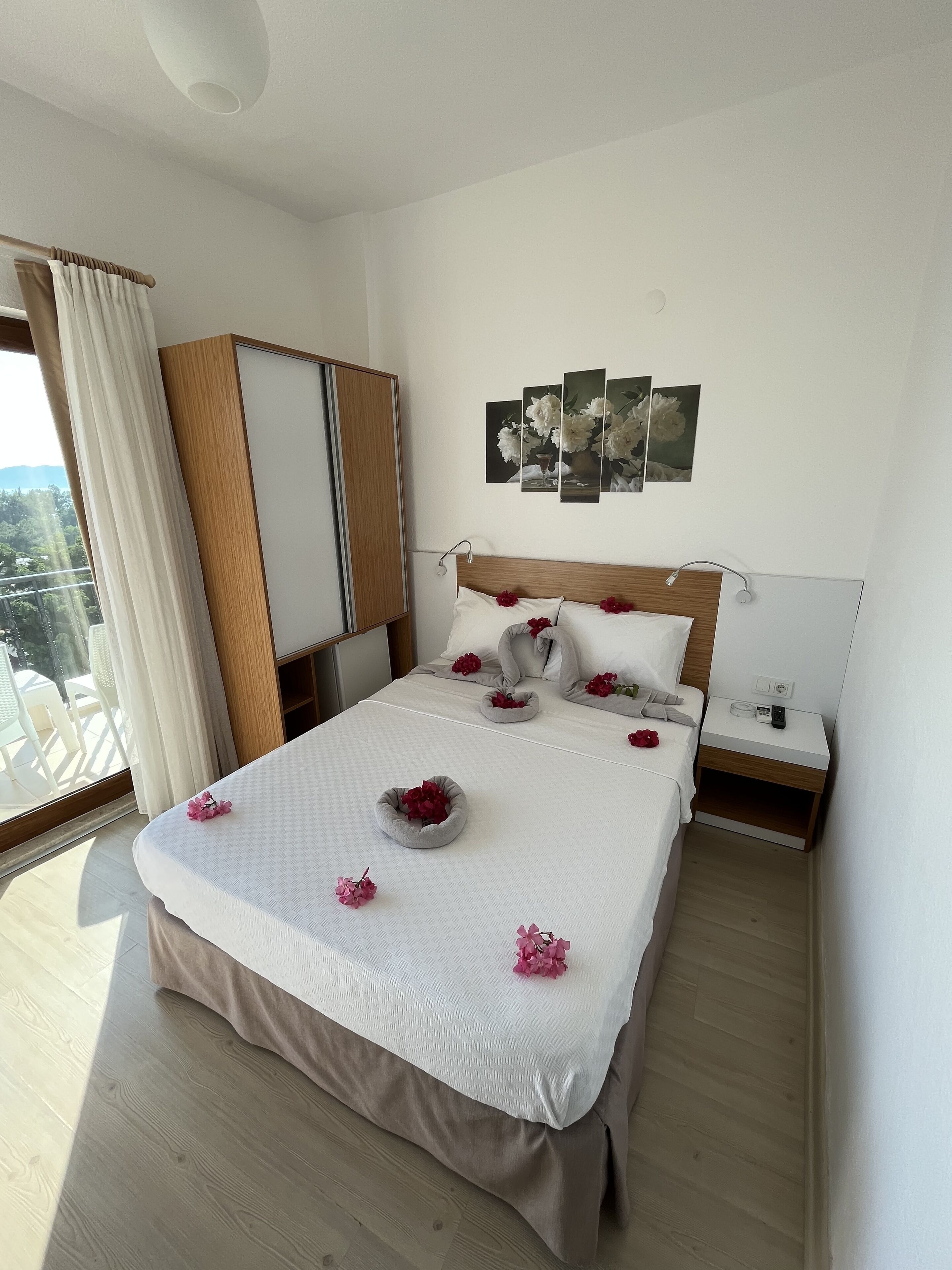 A hotel bedroom with a large bed, a wardrobe, a nightstand, and a wall-mounted artwork.