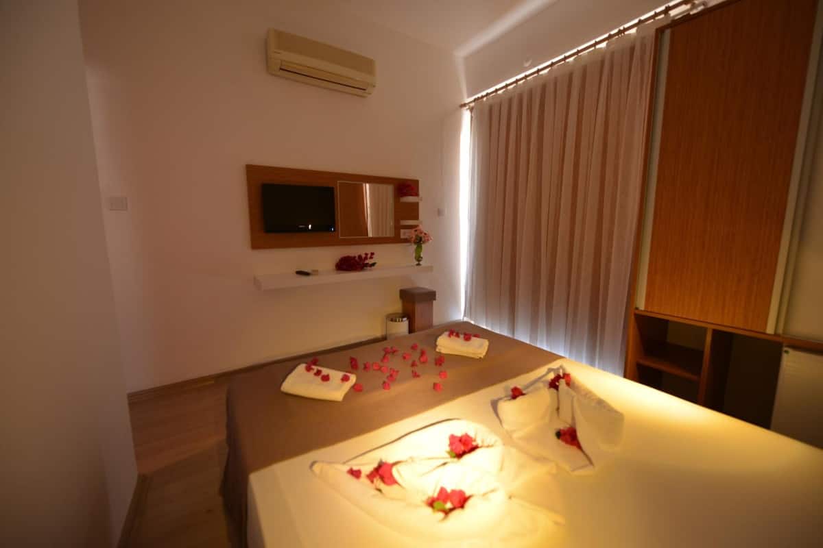 Une chambre d’hôtel avec un lit, une télévision, un miroir et une fenêtre avec des rideaux.