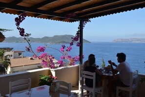 Eine Terrasse mit Meerblick, weißen Stühlen und einem Tisch mit einer kleinen Pflanze.