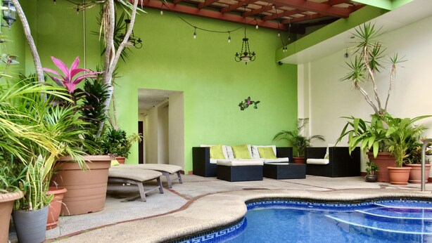 A pool area with lounge chairs, potted plants, and a green wall. - Hotel La Guaria Inn & Suites (Alajuela)