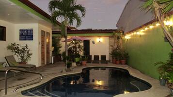 Relax by the pool surrounded by lush greenery and shaded by a comfortable umbrella.