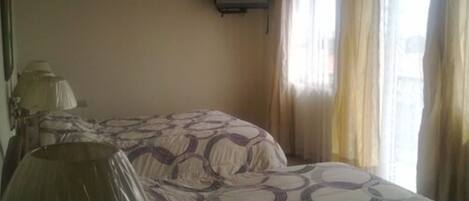 Habitación con dos camas, ventilador de techo, televisión montada en la pared y ventana con cortinas.