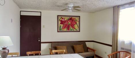 Habitación de hotel con una mesa de comedor, sillas, un sofá, un ventilador de techo y un cuadro grande con motivos florales en la pared.