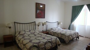 A room with two beds, a ceiling fan, a painting on the wall, and a window with curtains. - Hotel La Guaria Inn & Suites (Alajuela)