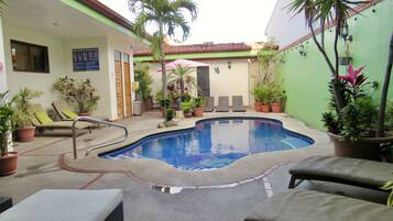 Un área de piscina con sillas de descanso, una piscina pequeña y plantas en macetas.