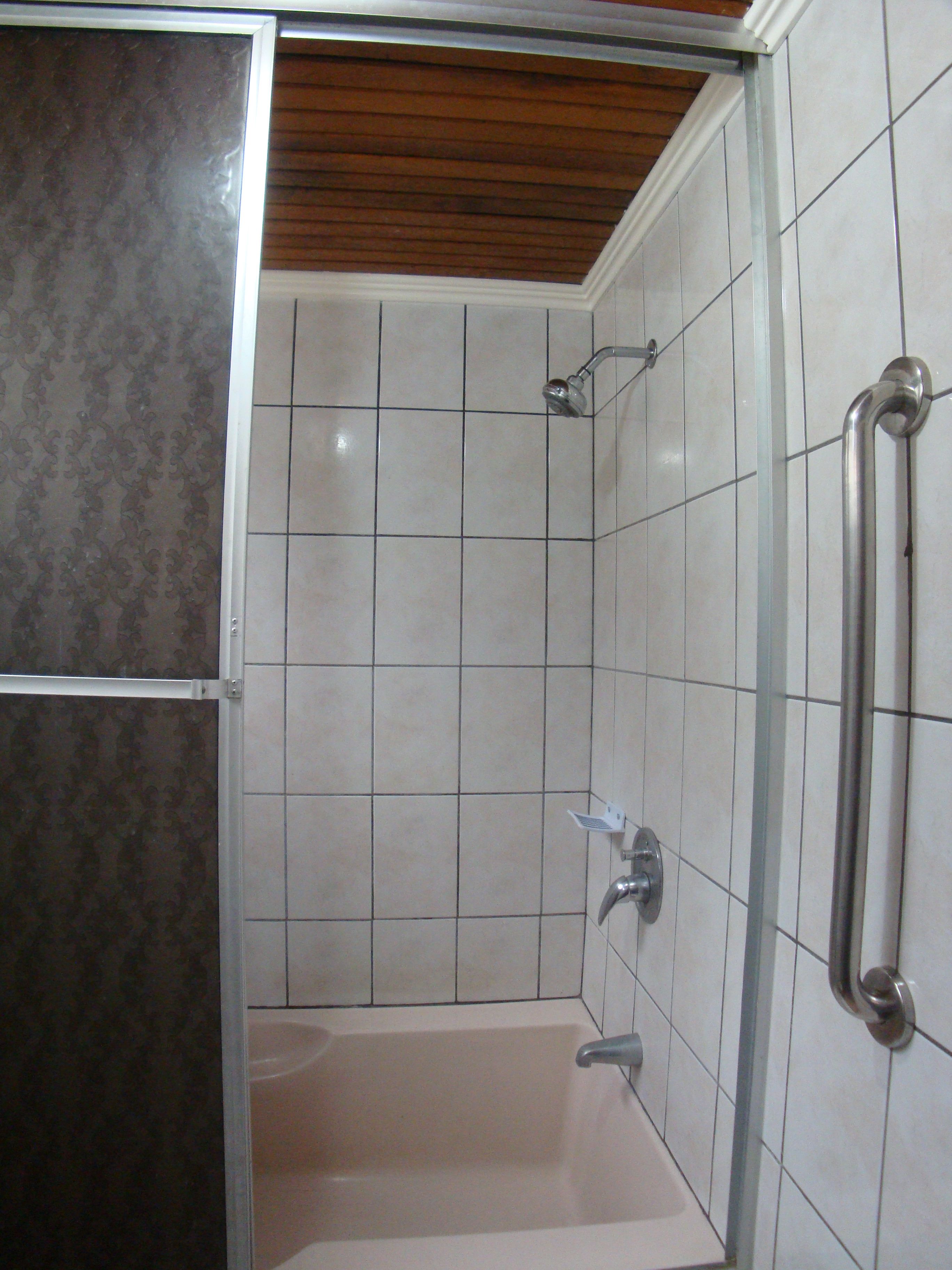 A shower area with a bathtub, tiled walls, and a wooden ceiling.