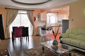 Uma sala de estar moderna com uma mesa de centro de vidro, um sofá e uma área de refeições com cadeiras.