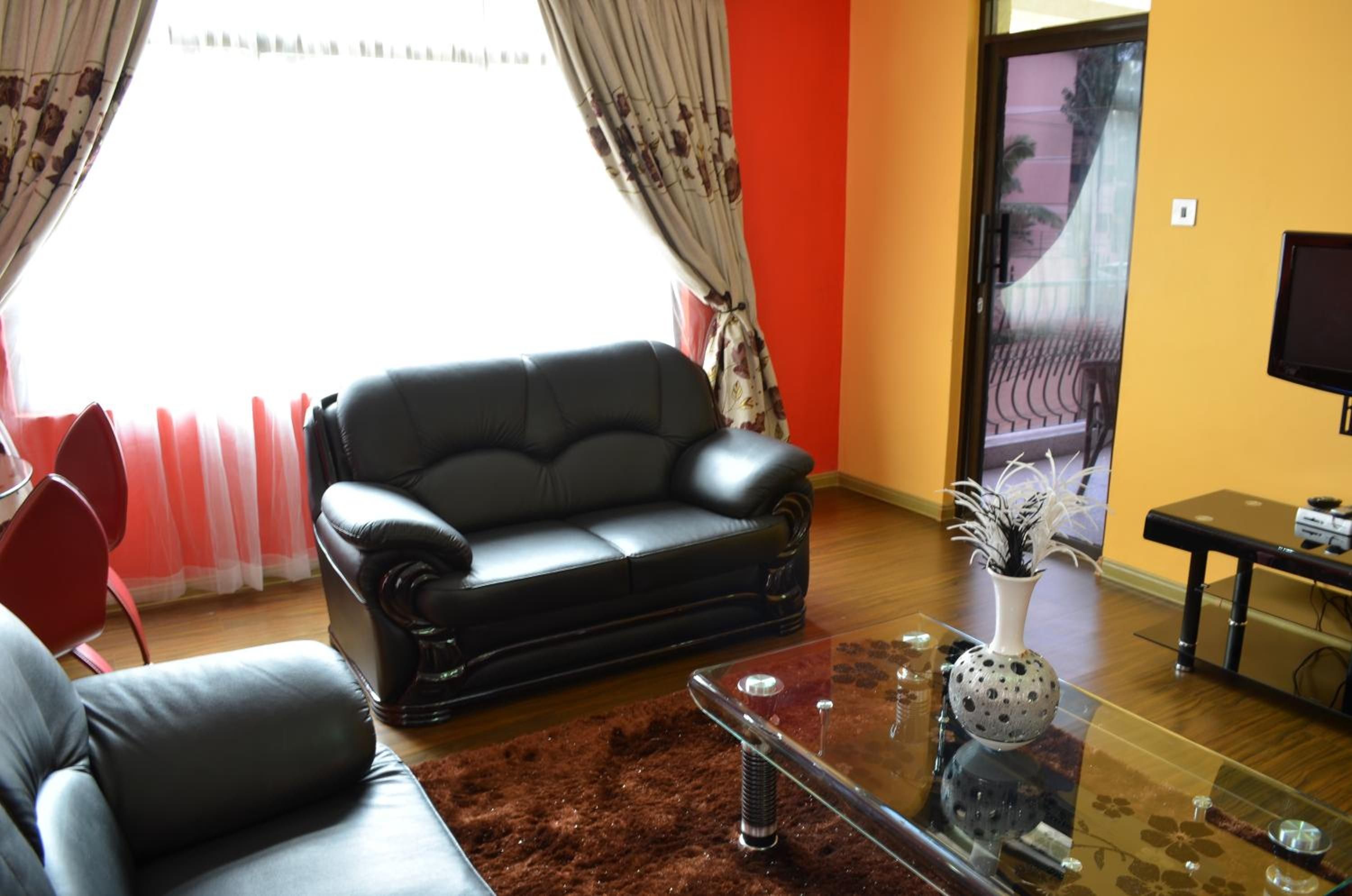 A living room with a black leather sofa, a glass coffee table, and a red carpet.