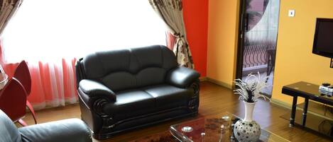 A living room with a black leather sofa, a glass coffee table, and a red carpet.