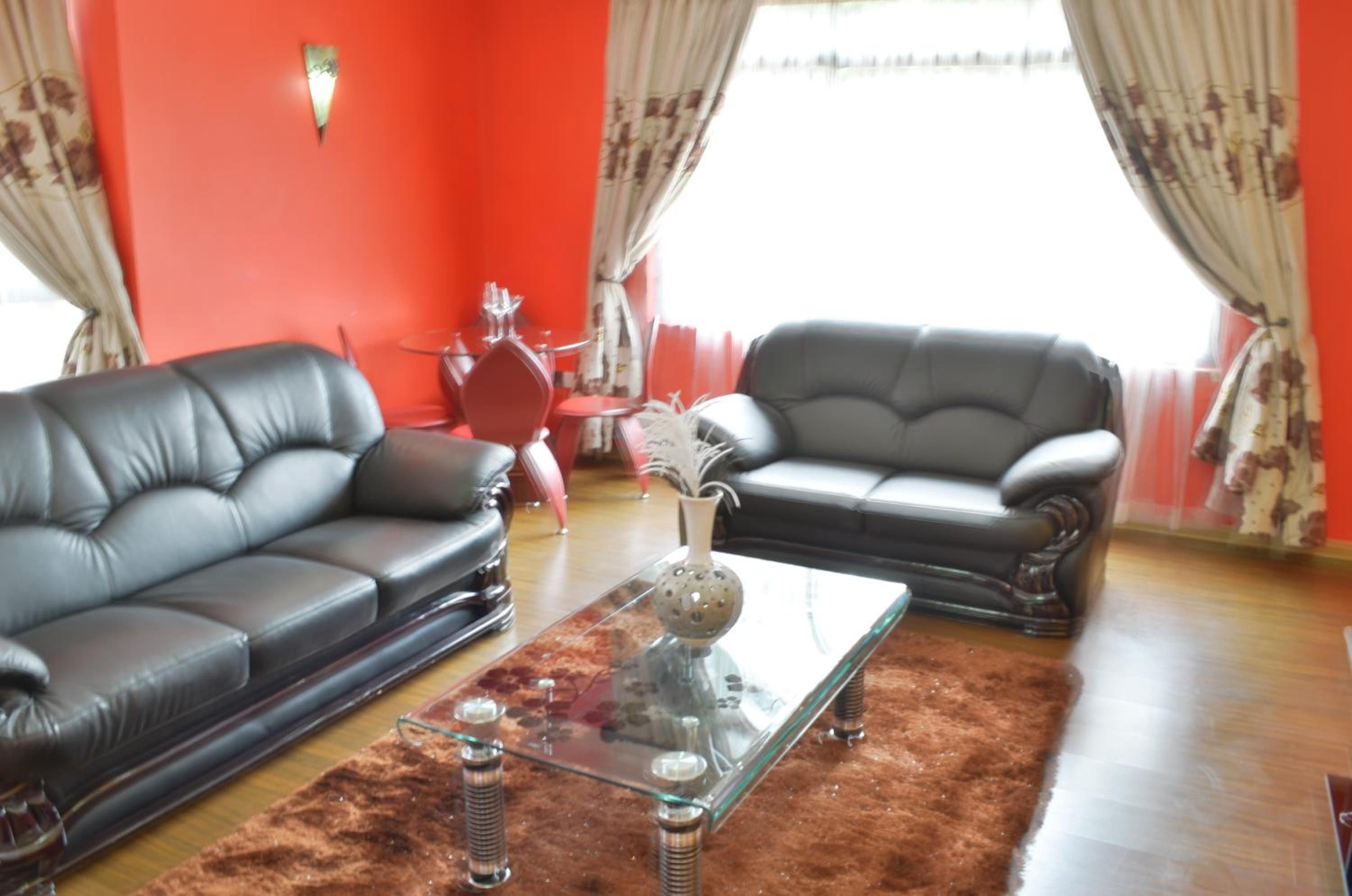 A living room with two leather sofas, a glass coffee table, and a red wall.