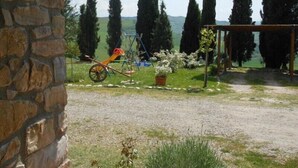 En stenmur, en skottkärra och en trädgård med höga träd och en pergola.