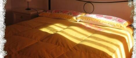 A bed with a yellow bedspread and floral pillows, a bedside table with a lamp, and a headboard with a circular design.