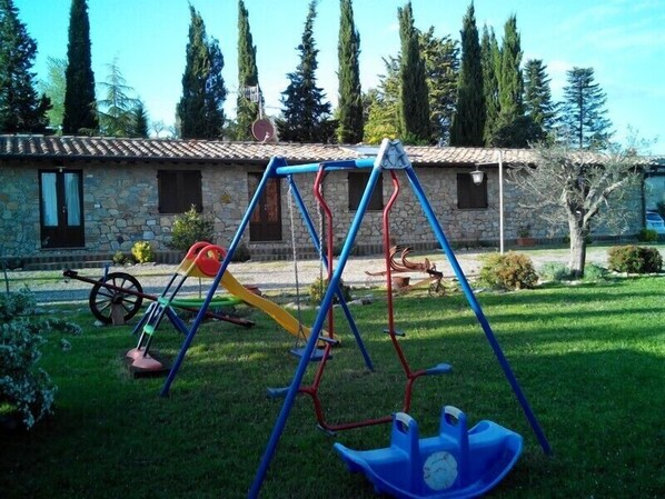 Un patio de juegos con columpios y un tobogán frente a un edificio de piedra con tejado de baldosas.