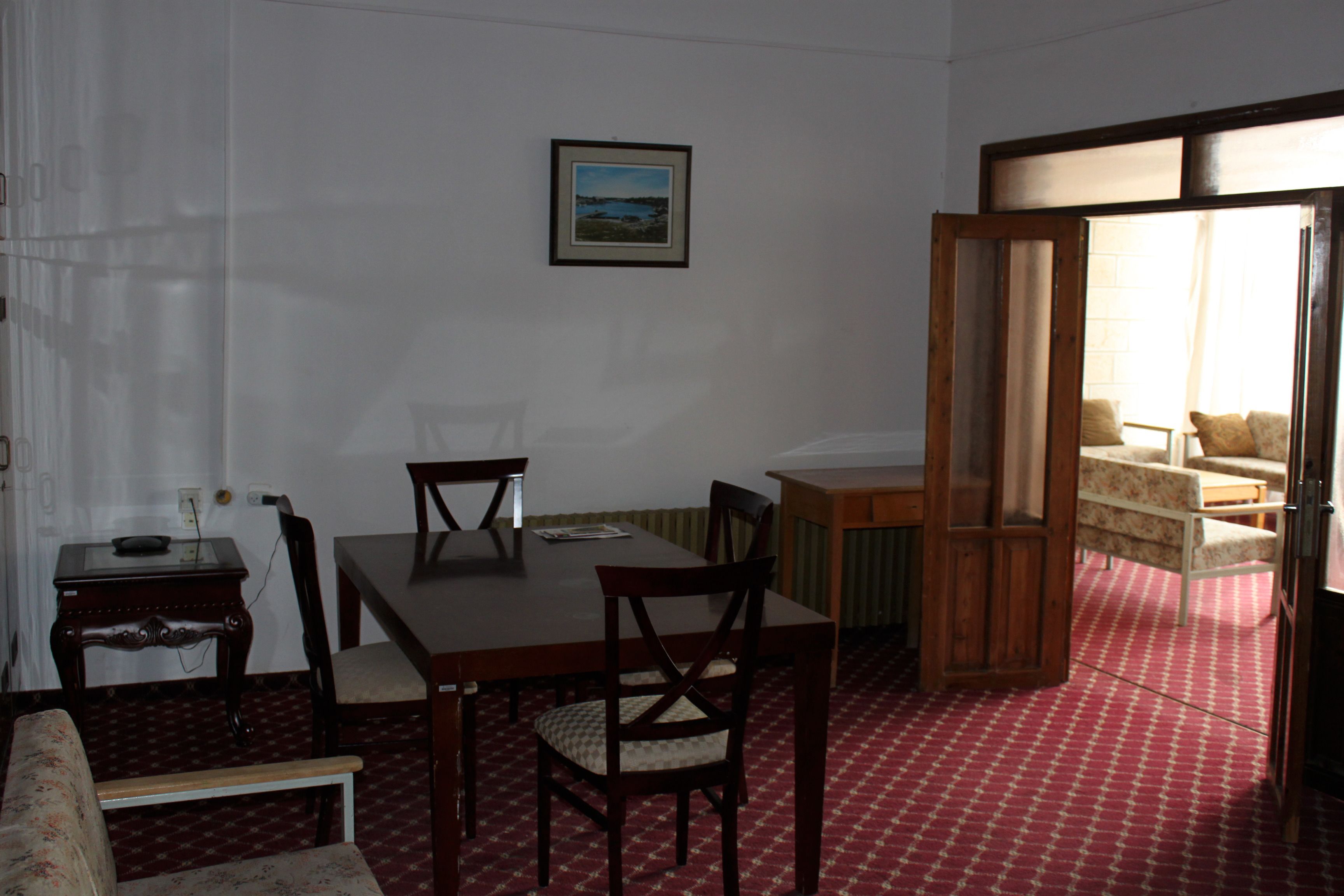 A dining area with a wooden table and chairs, a small side table, and a framed picture on the wall.