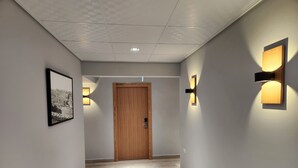 Un couloir avec une porte en bois, des luminaires fixés aux murs et un tableau encadré sur le côté gauche.