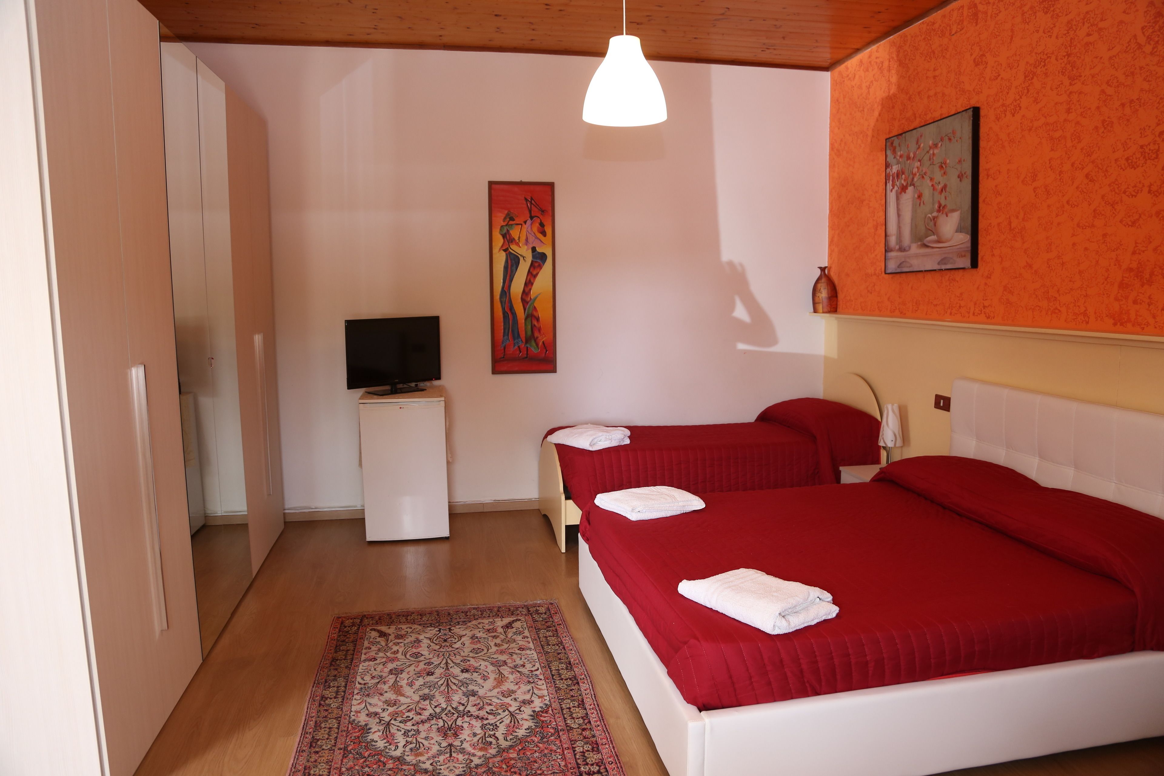 A hotel room with two beds, a television, a painting, and a patterned rug.