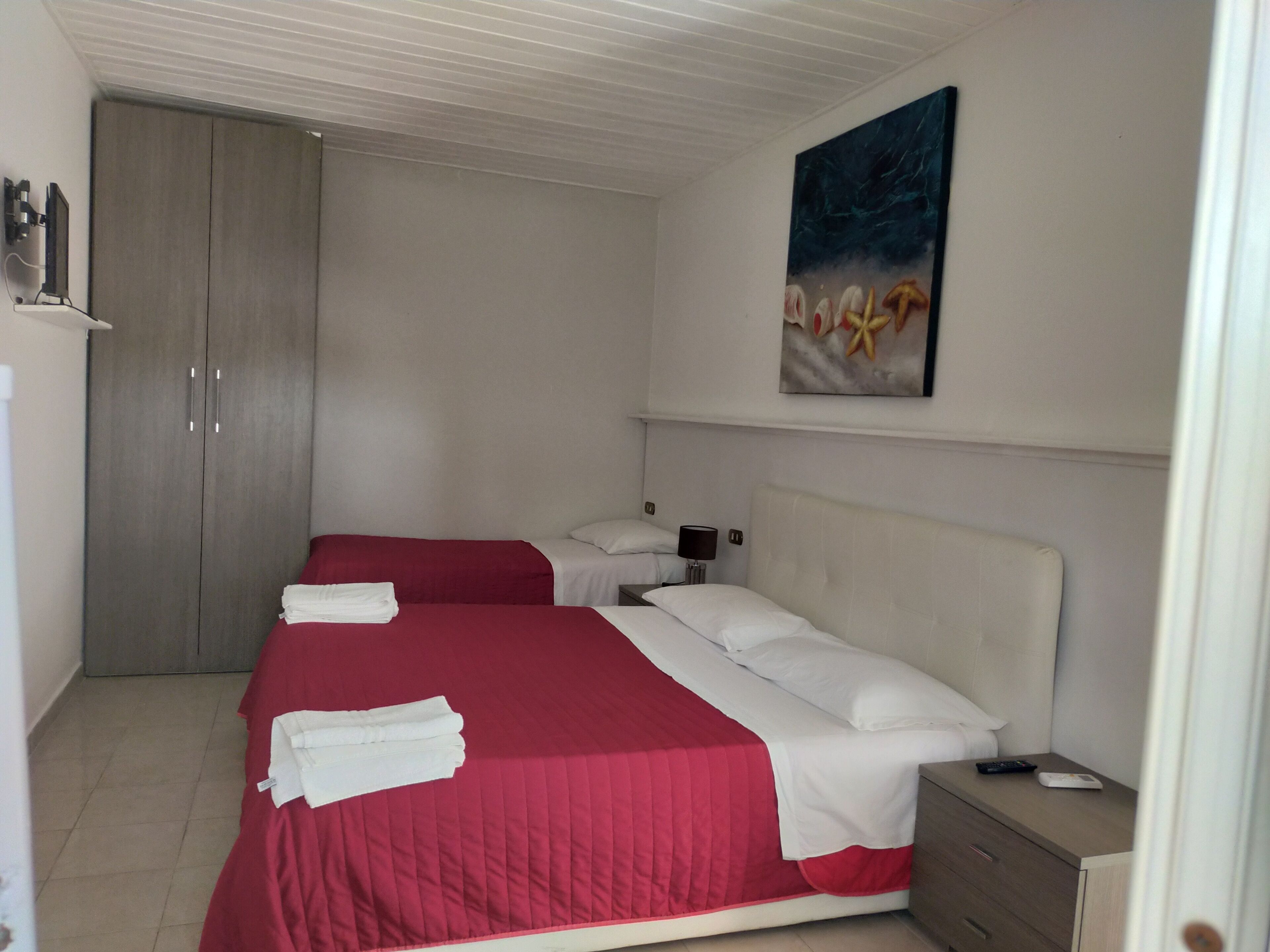 Quarto de hotel com duas camas, um guarda-roupa, uma mesa de cabeceira e um quadro na parede.