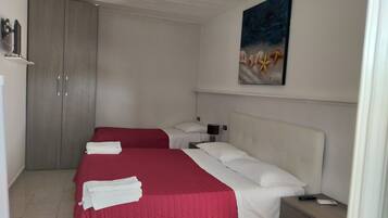 Quarto de hotel com duas camas, um guarda-roupa, uma mesa de cabeceira e um quadro na parede.