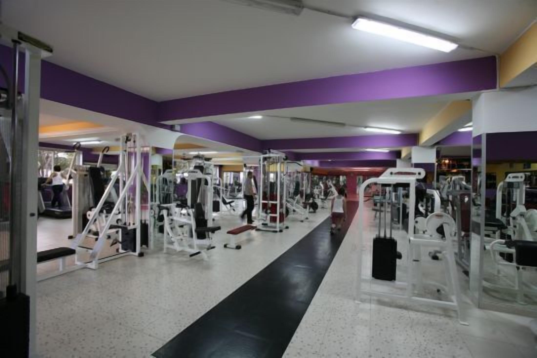 Una palestra con diverse macchine per esercizi, un percorso pedonale centrale e pareti viola.