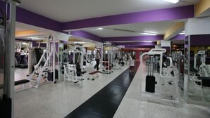 Ein Fitnessstudio mit verschiedenen Trainingsgeräten, einem zentralen Gehweg und violetten Wänden.