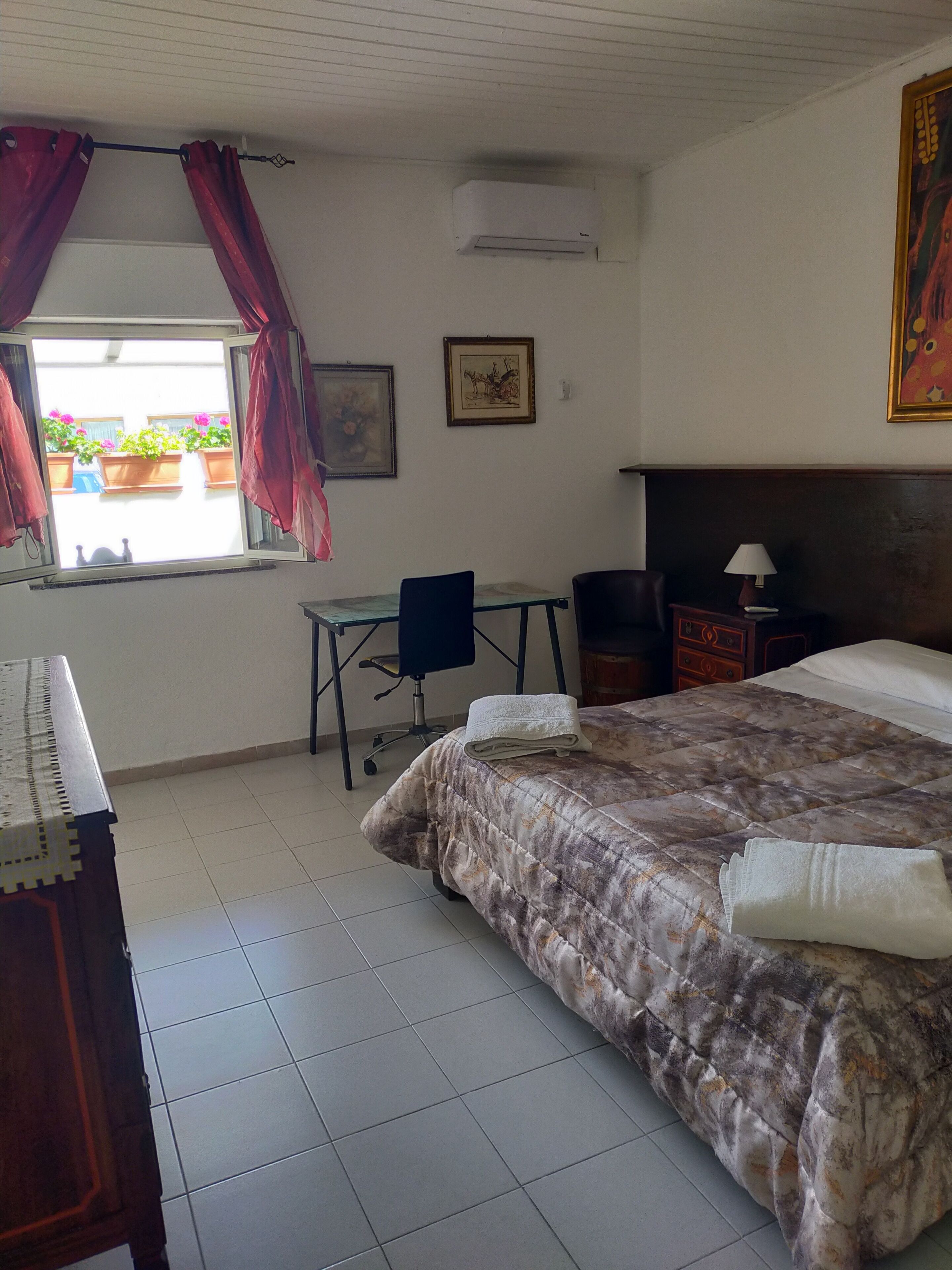Un dormitorio con cama, escritorio, silla, mesita de noche y ventana con cortinas.