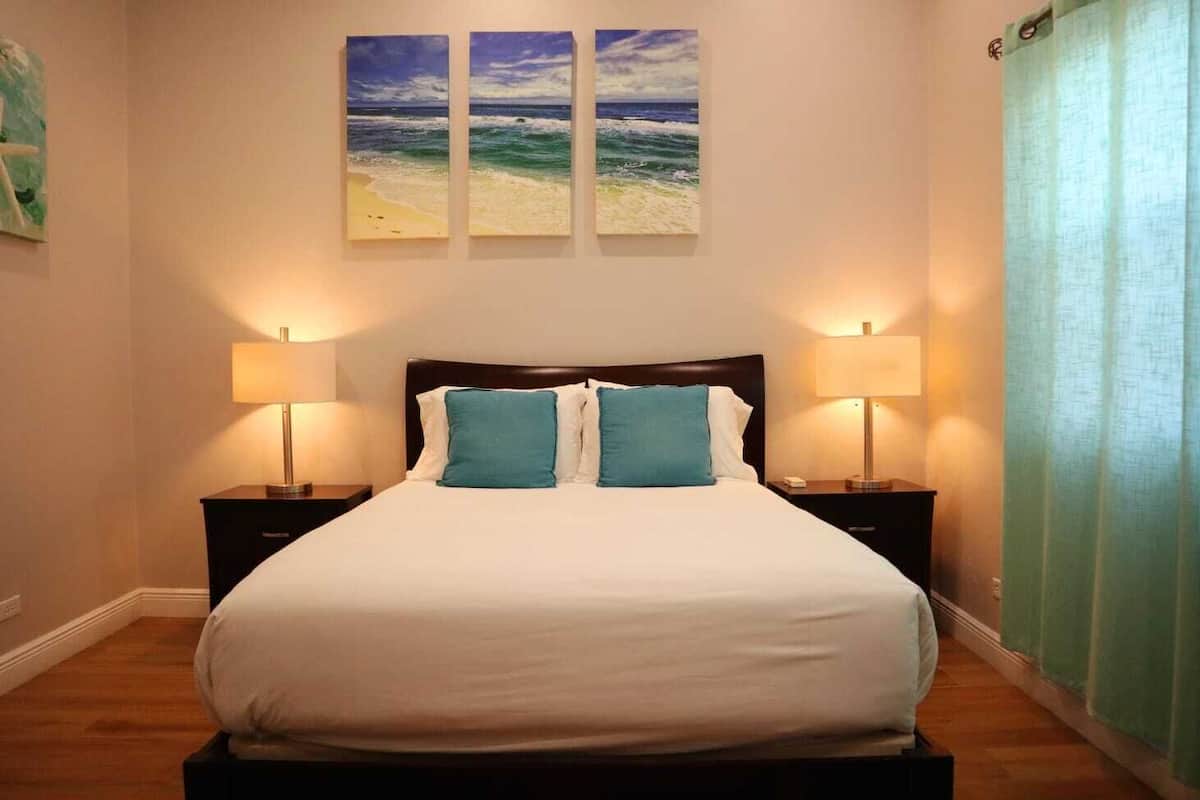 Une chambre d’hôtel avec un grand lit, deux lampes de chevet et trois tableaux représentant l’océan accrochés au mur.