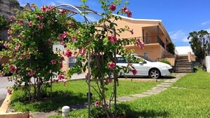 A residential area with a white car parked in front of a building with a balcony. - Paraquet Apartments (Paget Parish)