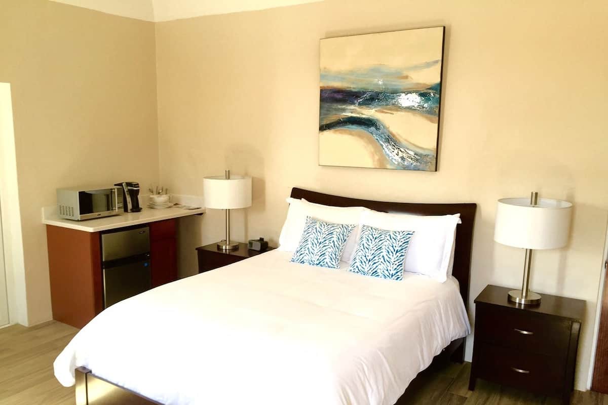 Une chambre d’hôtel avec un grand lit, deux tables de chevet avec des lampes, un bureau avec un micro-ondes et un tableau au mur.