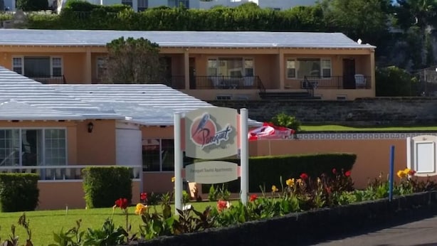A building with a sign for "Porquet Tourist Apartments" and a patio area with a red umbrella. - Paraquet Apartments (Paget Parish)