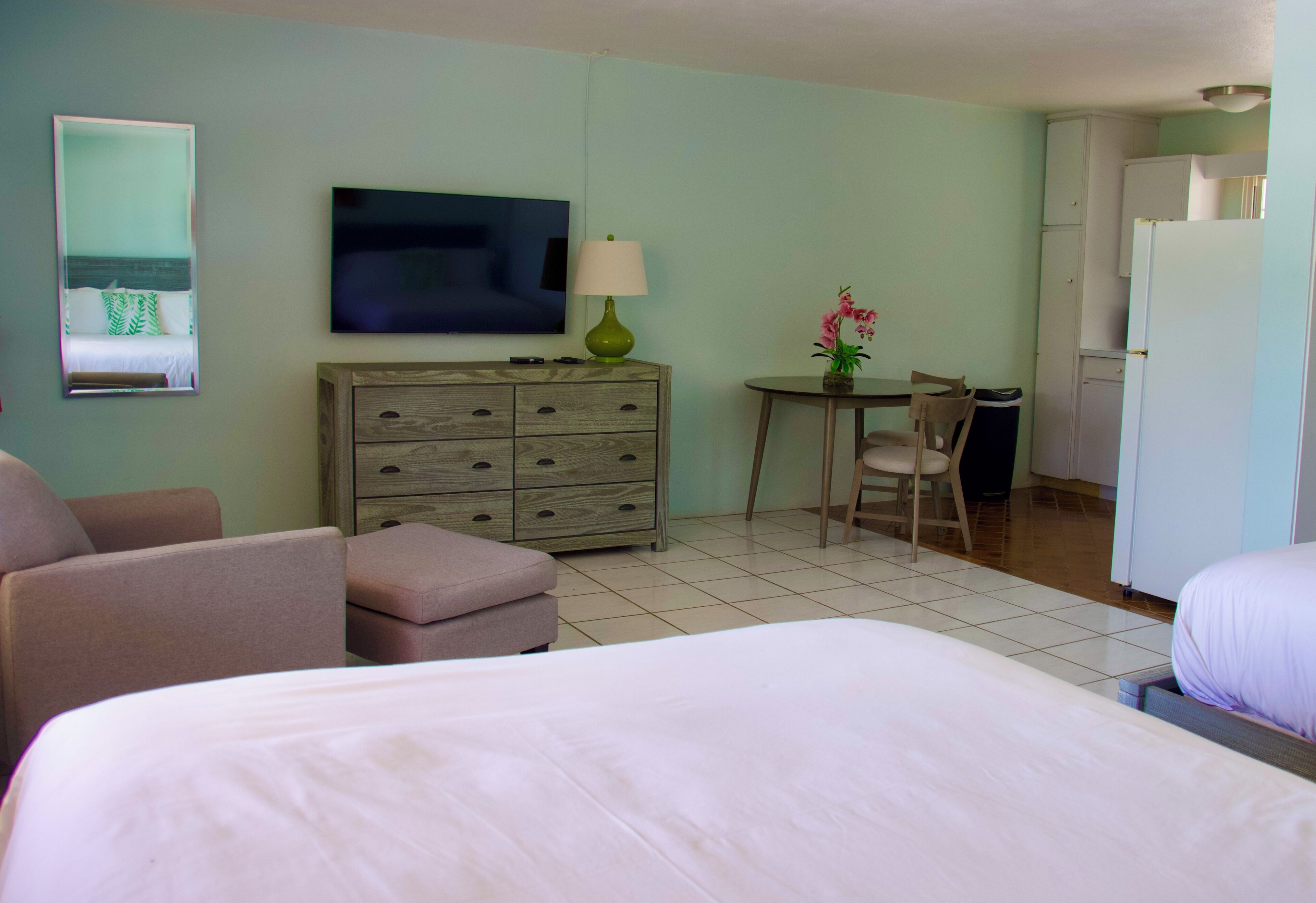 A hotel room with a bed, a desk, a chair, a television, a dresser, and a refrigerator.