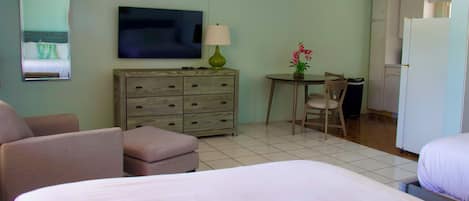 Habitación de hotel con cama, escritorio, silla, televisor, cómoda y refrigerador.