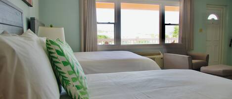 A hotel room with two beds, a chair, a desk, and a window with curtains.