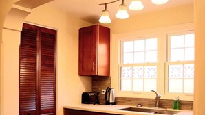 A kitchen with wooden cabinets, a countertop, a sink, and a window with decorative glass. - Paraquet Apartments (Paget Parish)