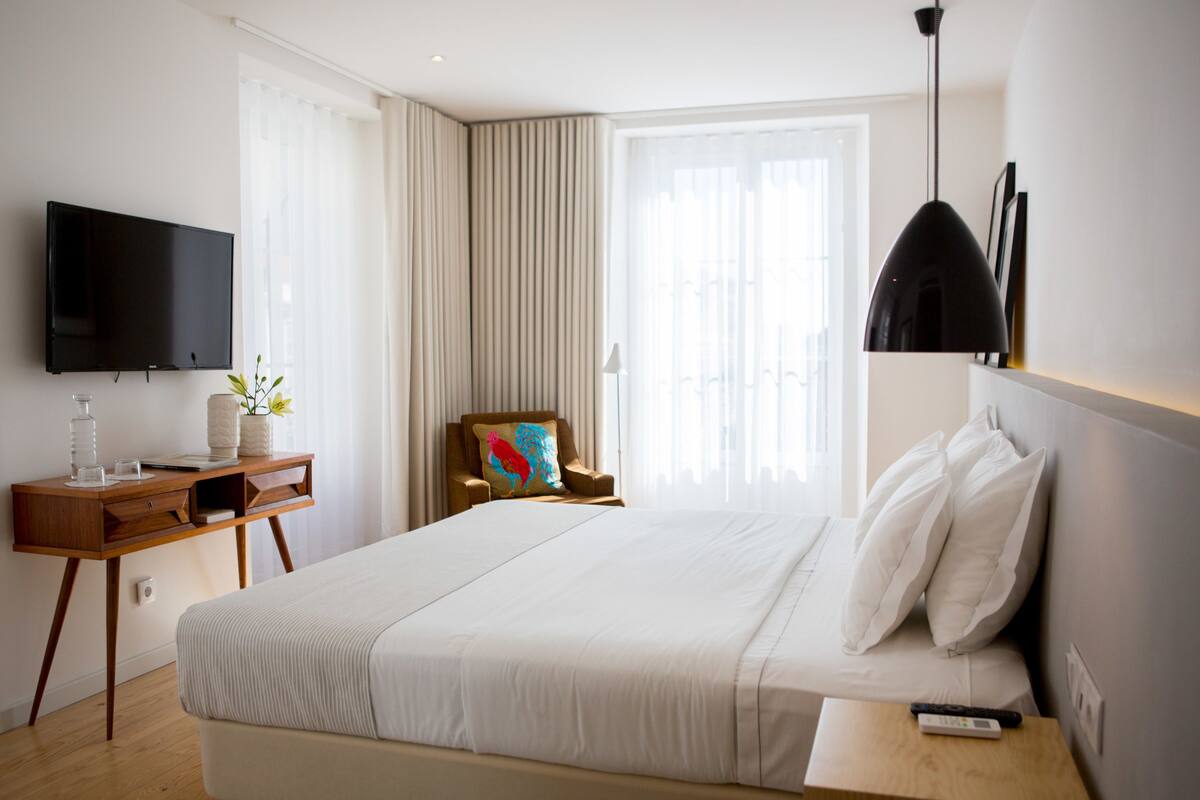Une chambre d’hôtel avec un grand lit, un bureau doté d’un téléviseur à écran plat, une chaise et une table de chevet avec une télécommande.