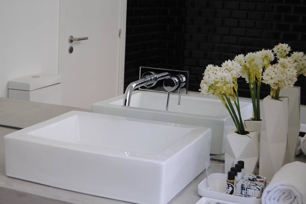 Une salle de bain moderne avec un grand lavabo rectangulaire, un lavabo plus petit et un miroir au-dessus du lavabo le plus petit. On y trouve un vase avec des fleurs blanches, une serviette et des articles de toilette sur le comptoir.