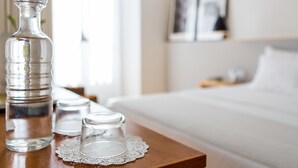 Habitación de hotel con una mesa ordenada que presenta una botella de vidrio transparente y dos recipientes de vidrio pequeños.