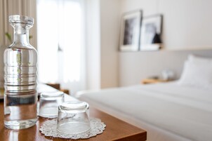 Quarto de hotel com uma mesa bem organizada, exibindo uma garrafa de vidro transparente e dois pequenos recipientes de vidro.
