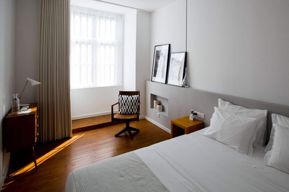 Une chambre d’hôtel avec un grand lit, un bureau avec une lampe, une chaise et une fenêtre avec des rideaux.