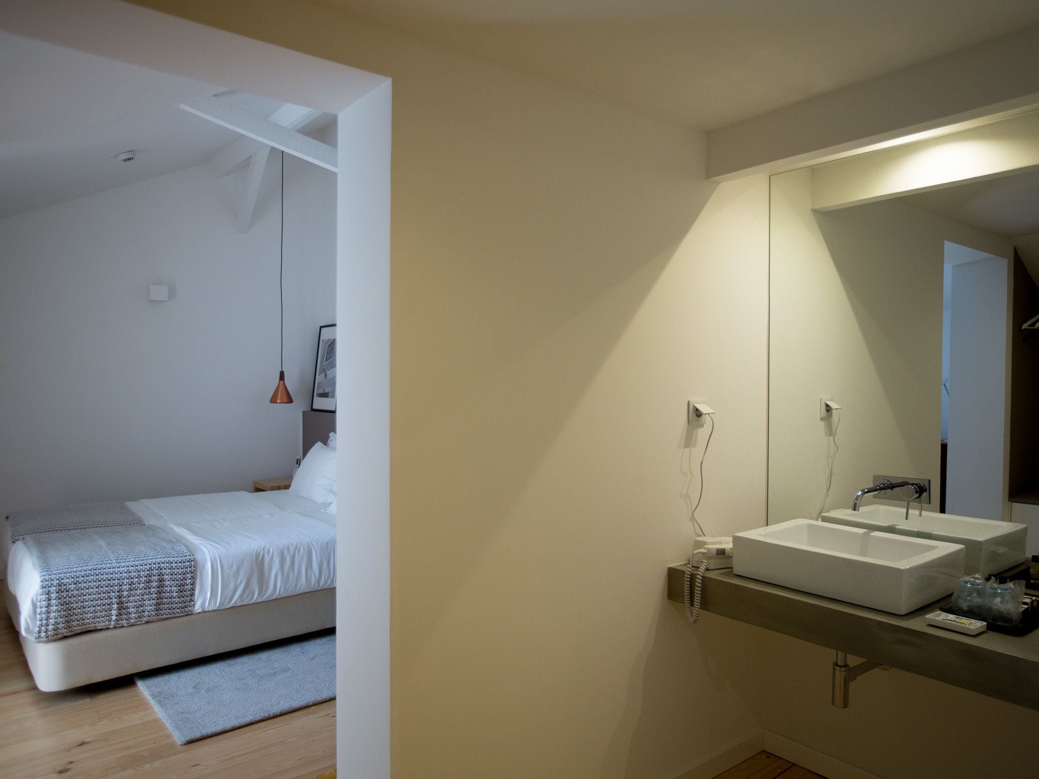 Un dormitori modern amb llit, una taula de nit i un mirall gran sobre el lavabo.