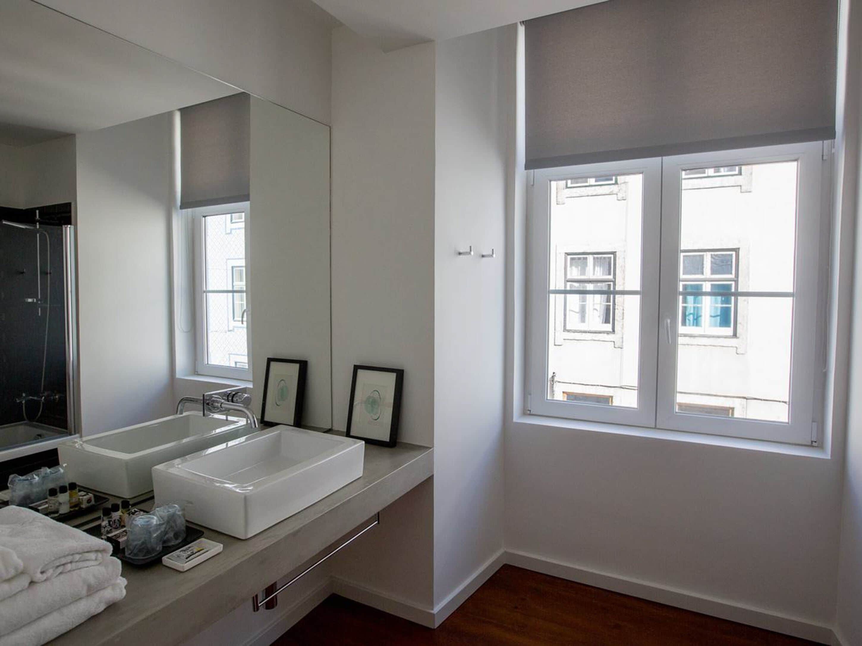 Une salle de bain moderne avec deux lavabos, un grand miroir et une fenêtre donnant sur des immeubles.