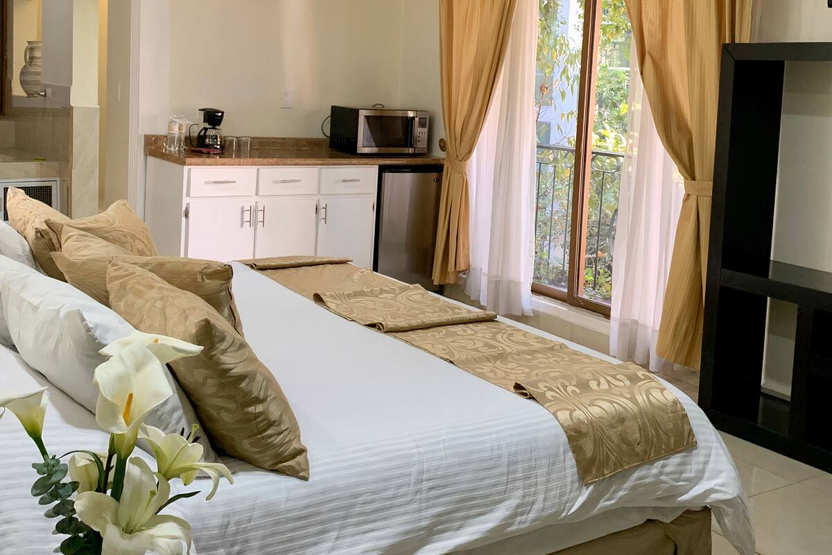 Una habitación de hotel con una cama grande, una kitchenette pequeña y un televisor.