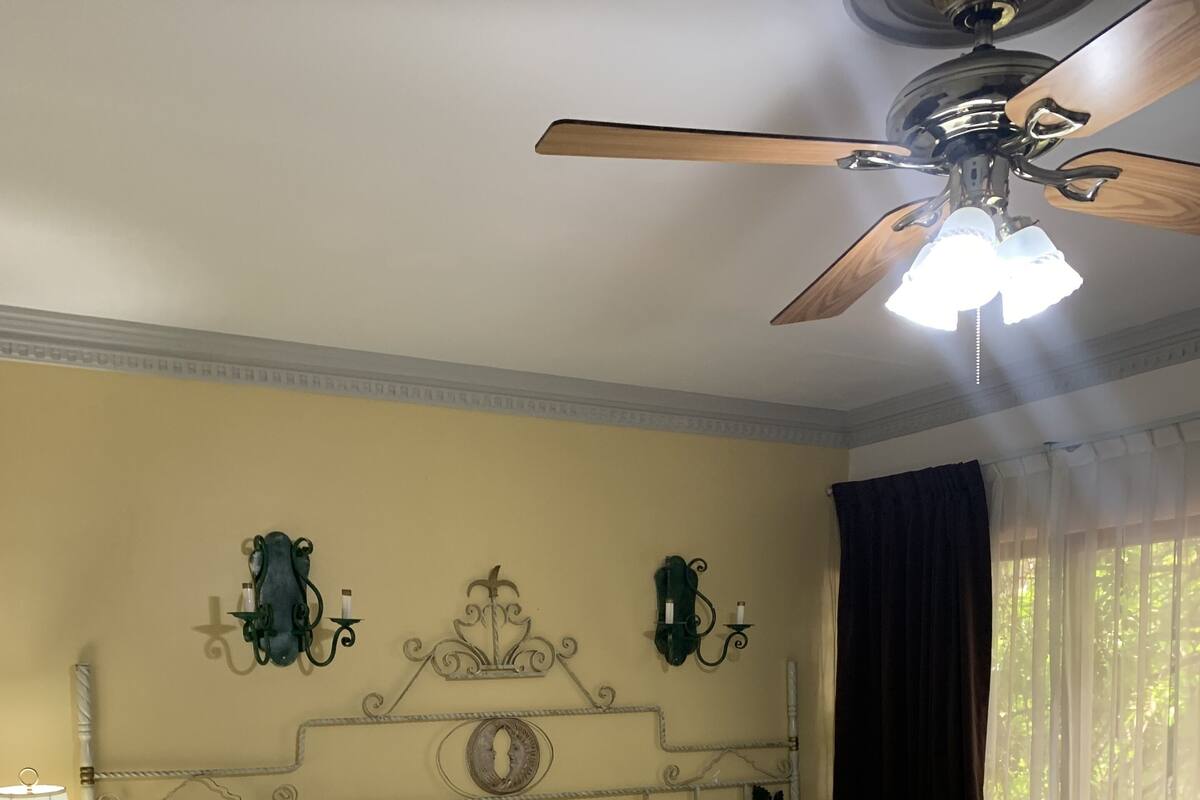 Una cama bien hecha con sábanas blancas, una mesita de noche con lámpara y un ventilador de techo.
