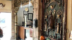 A reception area with a stone pillar, a glass-top table with decorative items, and a wall adorned with religious statues and carvings. - Inn Galerias Hotel (Aguascalientes)