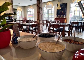 Un área de comedor con varias mesas y sillas, cuencos de comida y una planta en maceta.